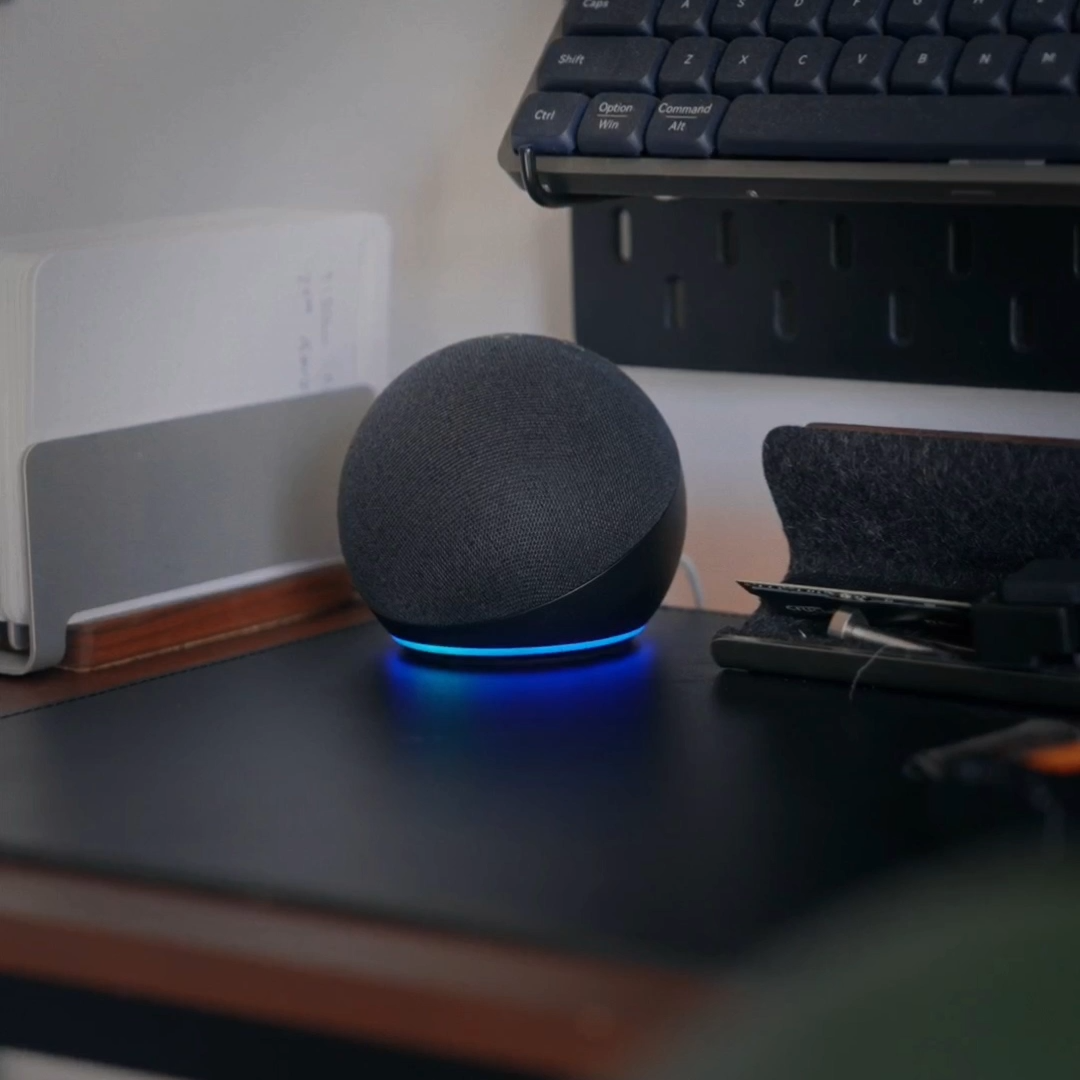 An Amazon Echo Dot with its blue light ring active on a desk, listening for a voice command