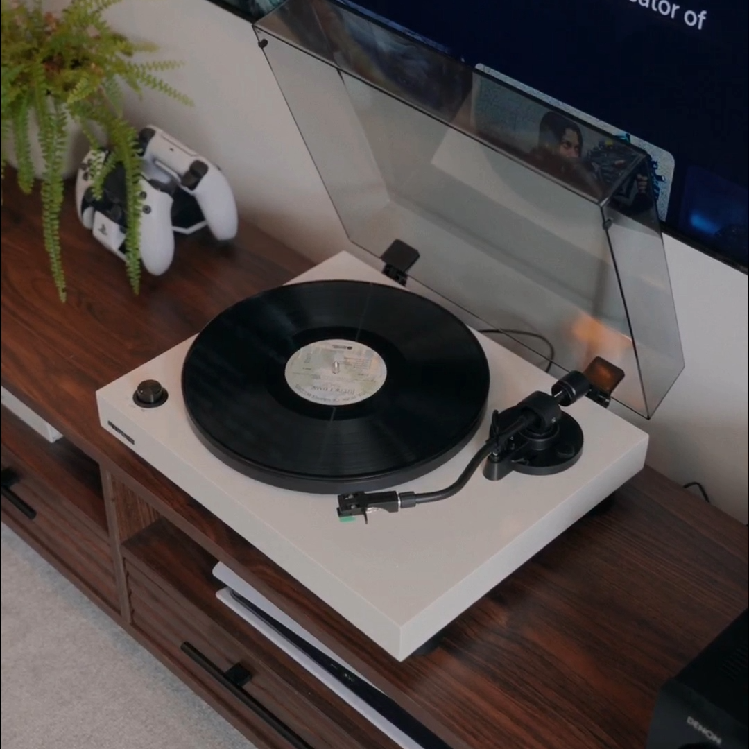 A vinyl record spinning on a turntable in a living room console with a TV behind it